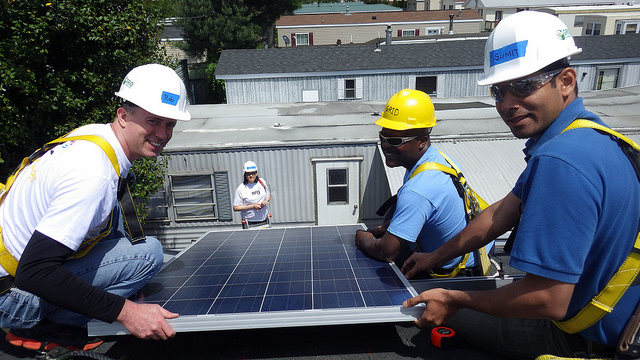 Four workers install solar panels on a residential rooftop during a sunny day