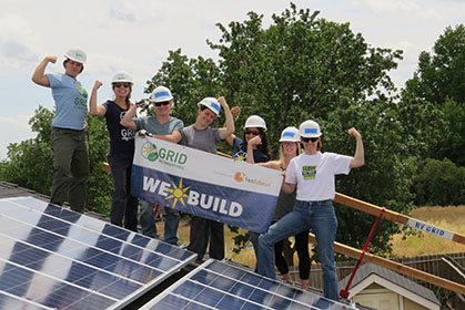 Group of women in hard hats celebrating solar panel installation with WeXBuild banner