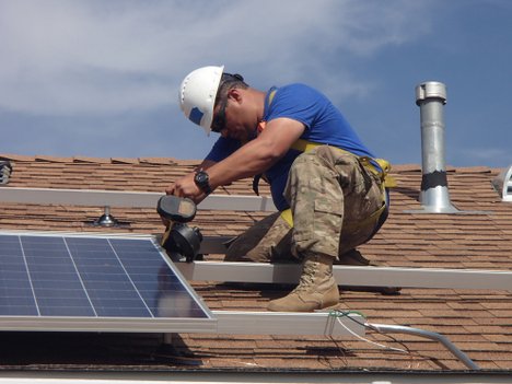 Worker in hard hat installing solar panel on residential roof