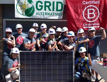 Team in hard hats holding a solar panel in front of Grid Alternatives and B Corporation logos