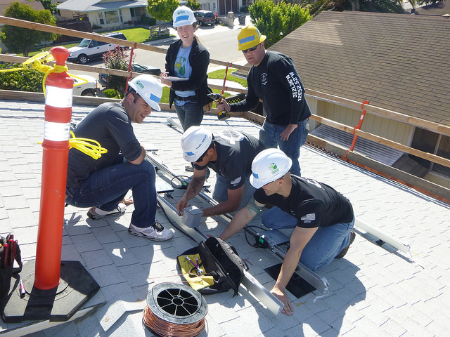Group of workers in hard hats installing roofing materials on a residential home during training