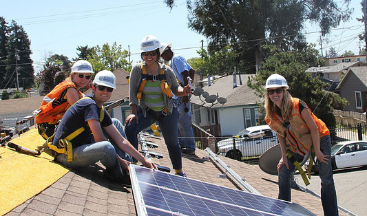 Workers in safety gear install solar panels on a residential rooftop during a sunny day
