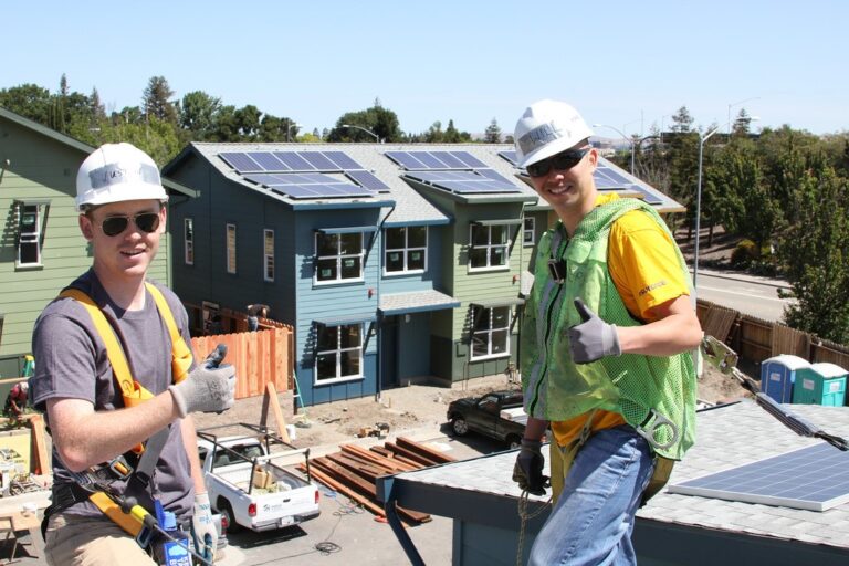 Two construction workers giving thumbs up in front of residential homes with solar panel installations
