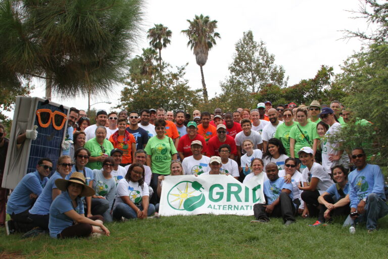 Large group holding GRID Alternatives banner at outdoor solar energy event in Orange County