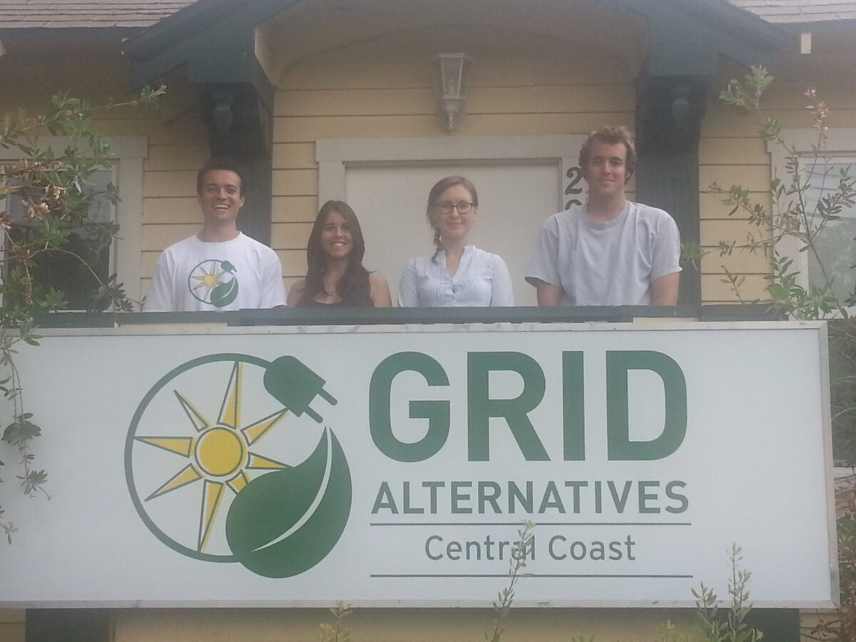 Four team members stand behind a GRID Alternatives Central Coast sign outside a house