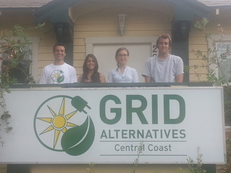 Four team members stand behind a GRID Alternatives Central Coast sign outside a house