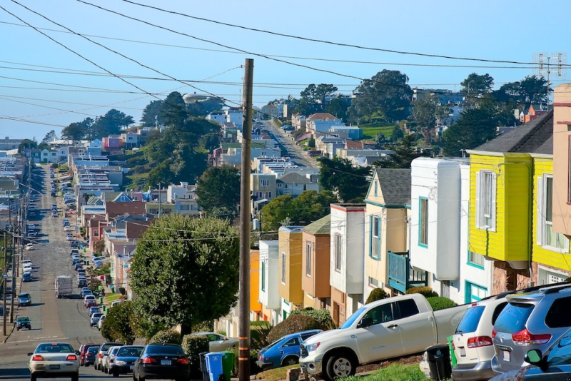 Colorful houses on a steep San Francisco street with parked cars and distant cityscape