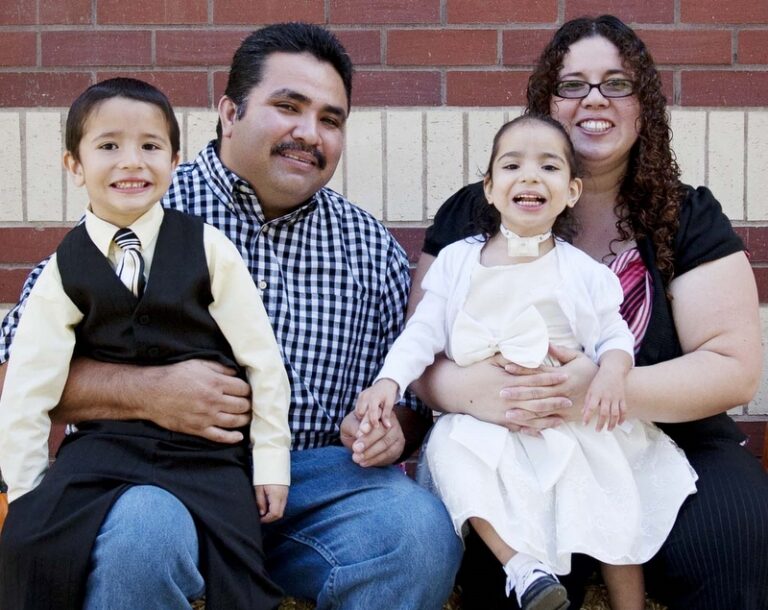 Family of four smiling together against a brick wall backdrop
