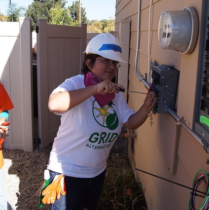 Technician in white hard hat and GRID Alternatives shirt installs solar equipment on residential panel