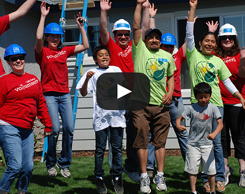 Diverse group of volunteers in red and green shirts with hard hats celebrating together outdoors
