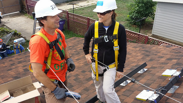 Two construction workers in safety gear and hardhats on a brick patio, discussing solar installation work