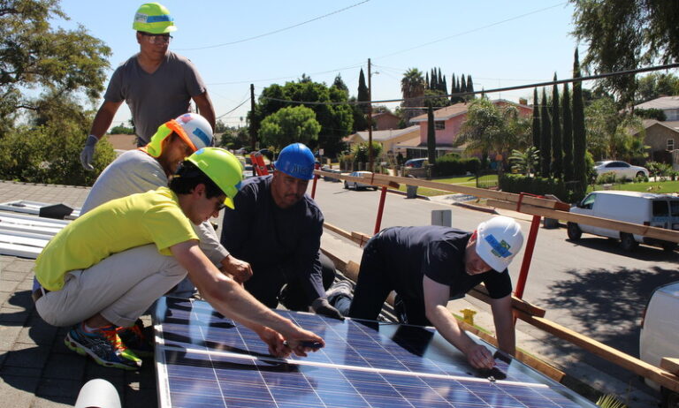 Construction workers install solar panels on a residential rooftop in Lynwood