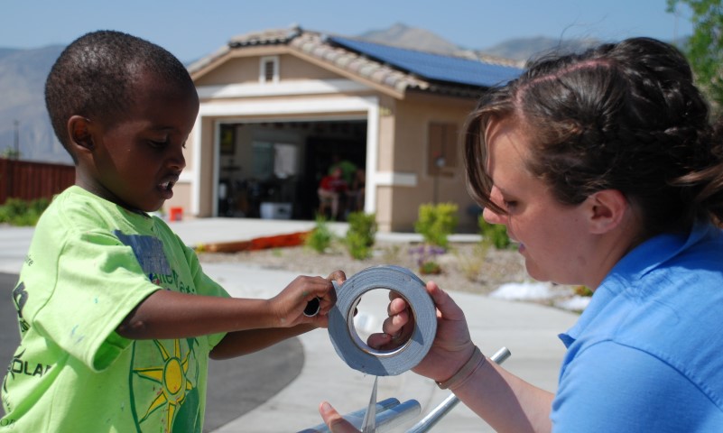 Adult and child holding a roll of tape outdoors in front of a house with solar panels