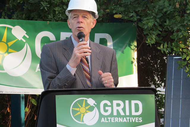 Man in hard hat speaking at podium with GRID Alternatives logo during solar event launch