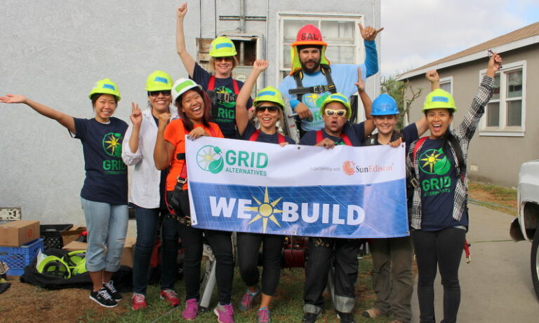 Group of volunteers in hard hats holding "We Build" banner at solar installation construction site