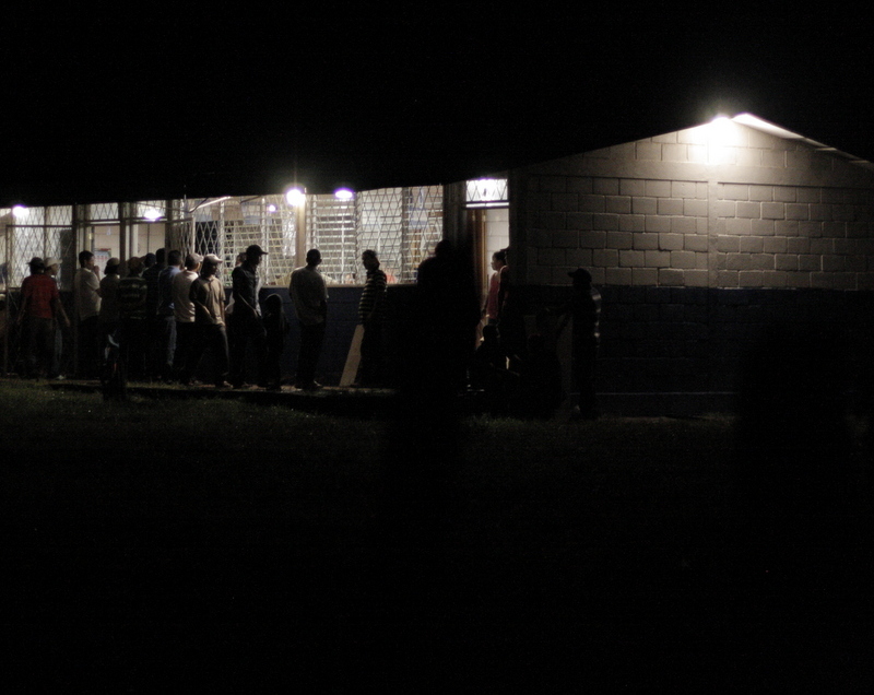 Group of people gathered outside illuminated building at night in rural Nicaragua