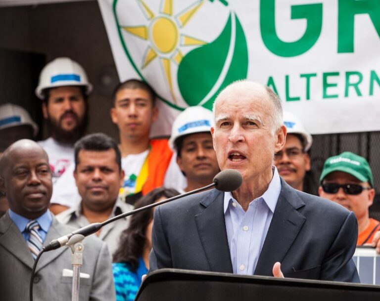 Man speaking at podium with green energy logo and workers behind him