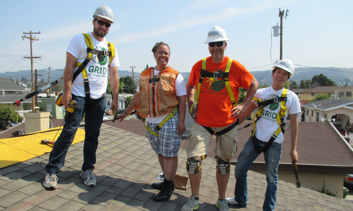 Five construction workers in safety gear smiling on a rooftop with mountains in background