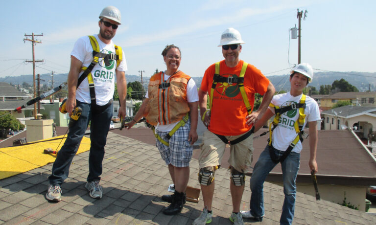 Five construction workers in safety gear smiling on a rooftop with mountains in background