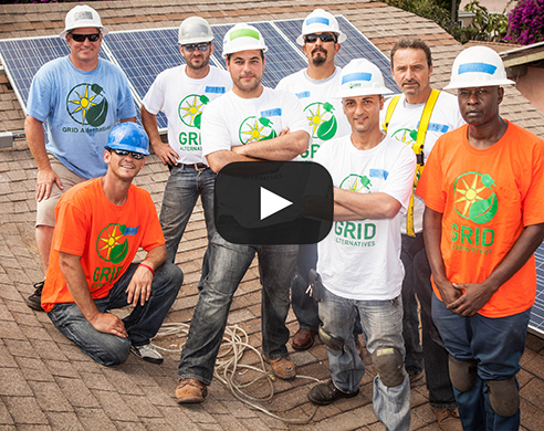 Team of workers in hard hats and GRID branded shirts posing on rooftop with solar panels