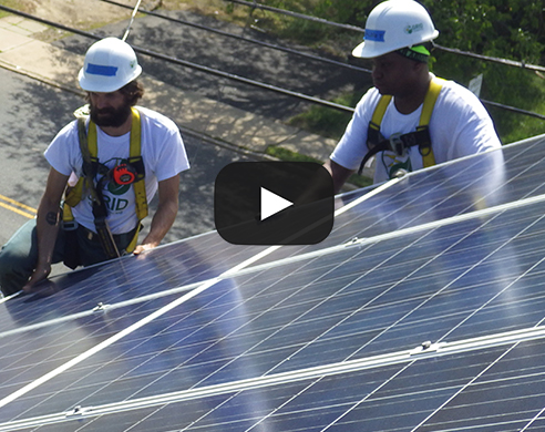 Two workers in hard hats installing solar panels on a roof during a rebuilding project