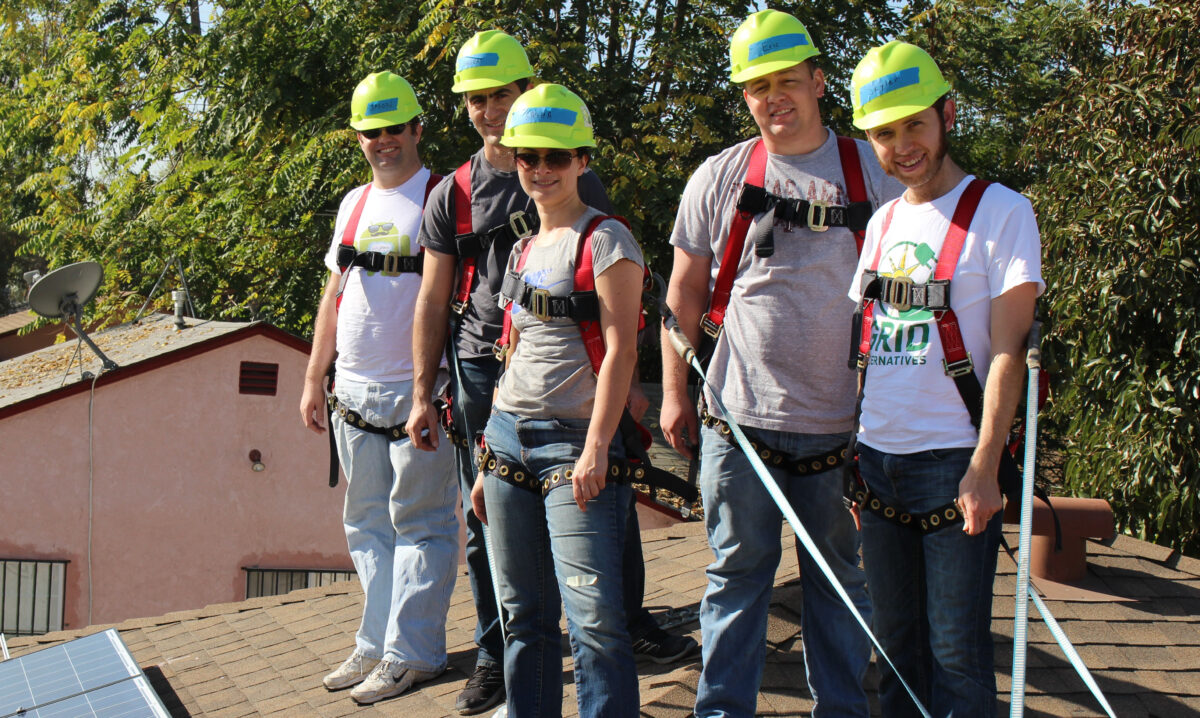Five safety-trained volunteers in hard hats and harnesses pose on a rooftop during a volunteer work project