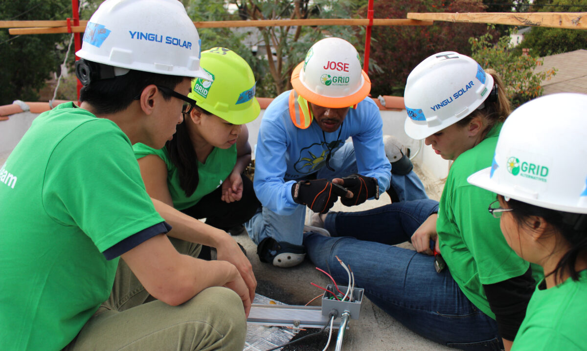 Team members in hard hats and green shirts gather around solar equipment during a training session