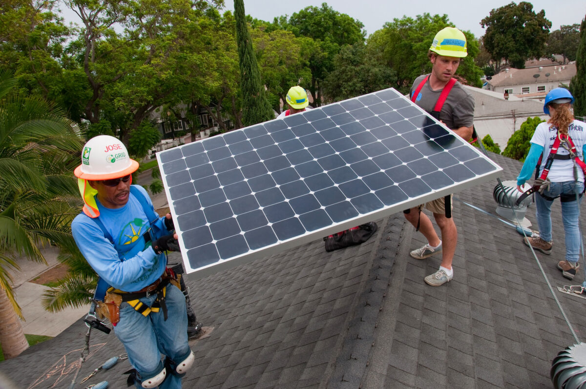 Workers installing a solar panel on a residential roof during a community installation event