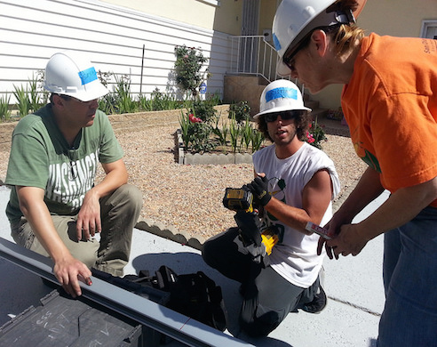 Three workers in hard hats examining roofing material during construction work outdoors