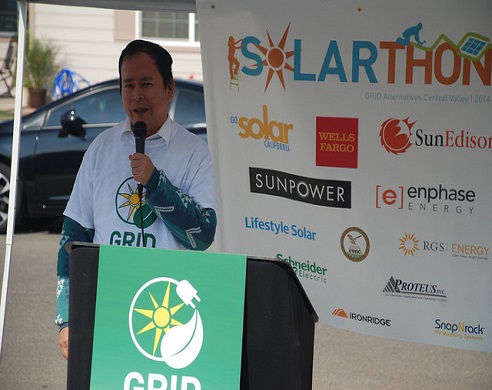 Man speaking at podium with GRID logo at Solarthon event with sponsor banners behind him