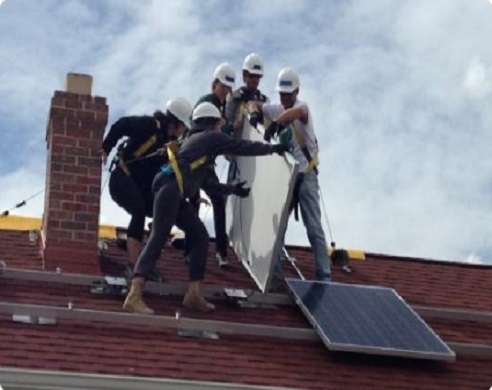 Workers in hard hats installing solar panels on a red roof