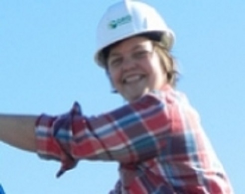 Smiling woman wearing white hard hat and red plaid shirt against blue sky