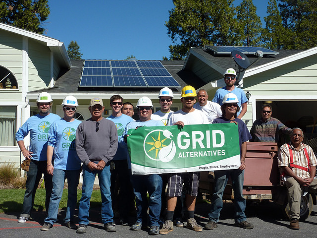 Group holding "Grid Alternatives" banner in front of house with solar panels on roof