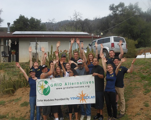 Group of volunteers with raised hands holding GRID Alternatives banner at solar installation site
