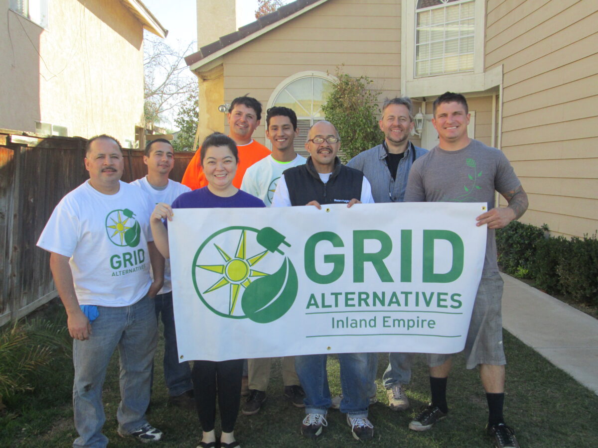 Seven people holding a GRID Alternatives Inland Empire banner in a residential backyard