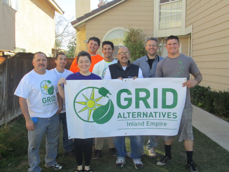 Seven people holding a GRID Alternatives Inland Empire banner in a residential backyard