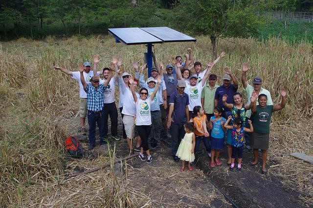 Group of people with raised arms standing under solar panels in a field