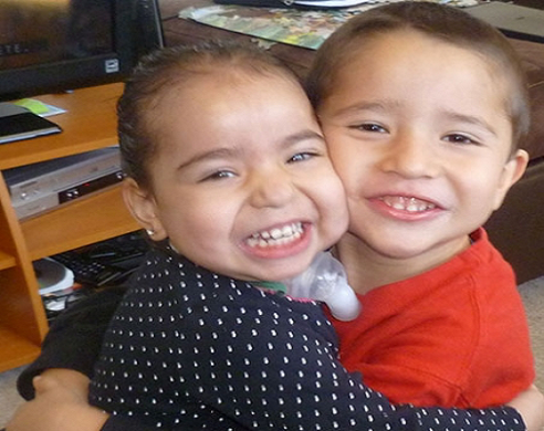 Two young children smiling at camera, one wearing black polka dot shirt, one in red shirt
