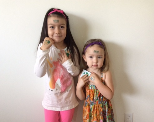 Two young girls with purple headbands standing against a white wall, smiling at the camera