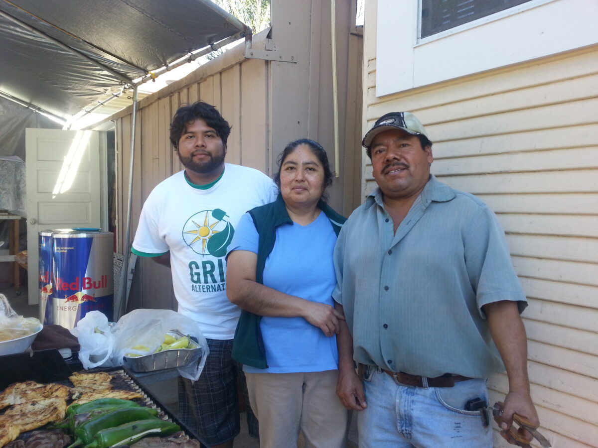 Three people standing together in a garage with food and drinks, demonstrating community cooperation and togetherness