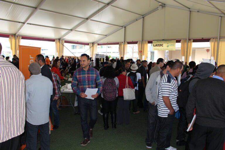 Large crowd gathered in tent venue with yellow curtains and signage, attending a job fair or event about solar energy careers