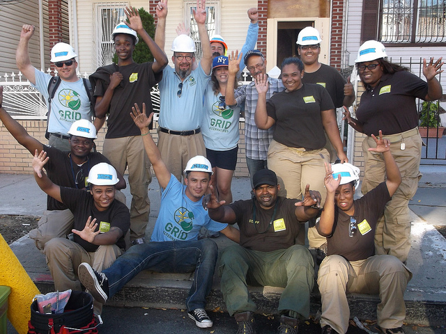 Group of diverse volunteers wearing hard hats and GRID shirts celebrate at a community solar initiative event