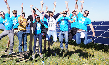 Group of volunteers with raised arms celebrating in front of solar panels