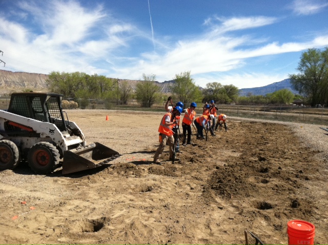 GRID's first community solar groundbreaking with workers in orange vests and construction equipment on a dirt field