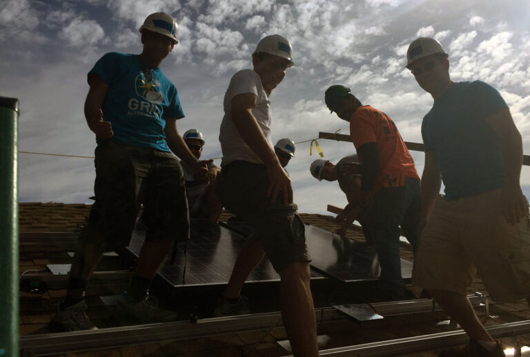 Construction crew installing solar panels on a rooftop under cloudy sky