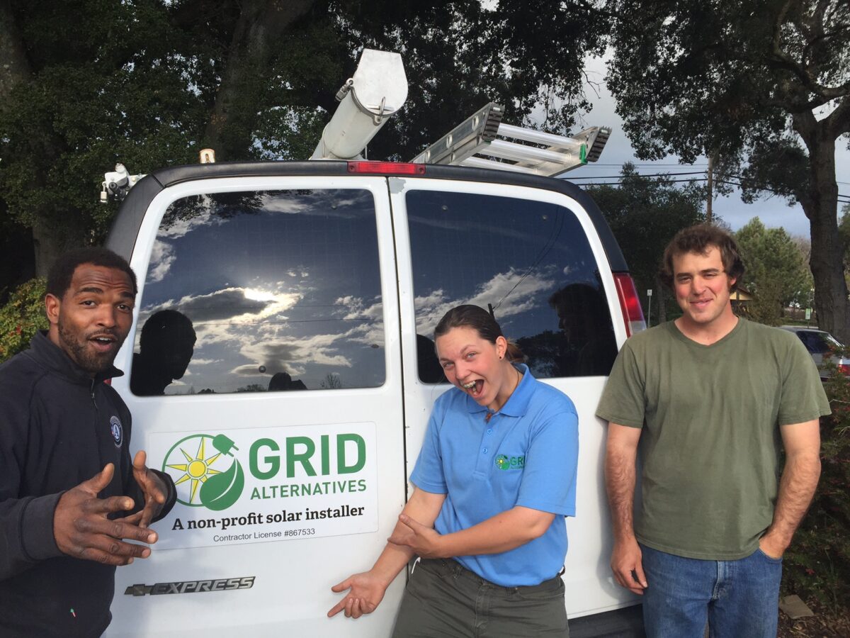 Three people pose in front of a white van labeled "Grid Alternatives, a non-profit solar installer