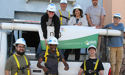 Team of workers in hard hats holding green GRID partnership banner at construction site
