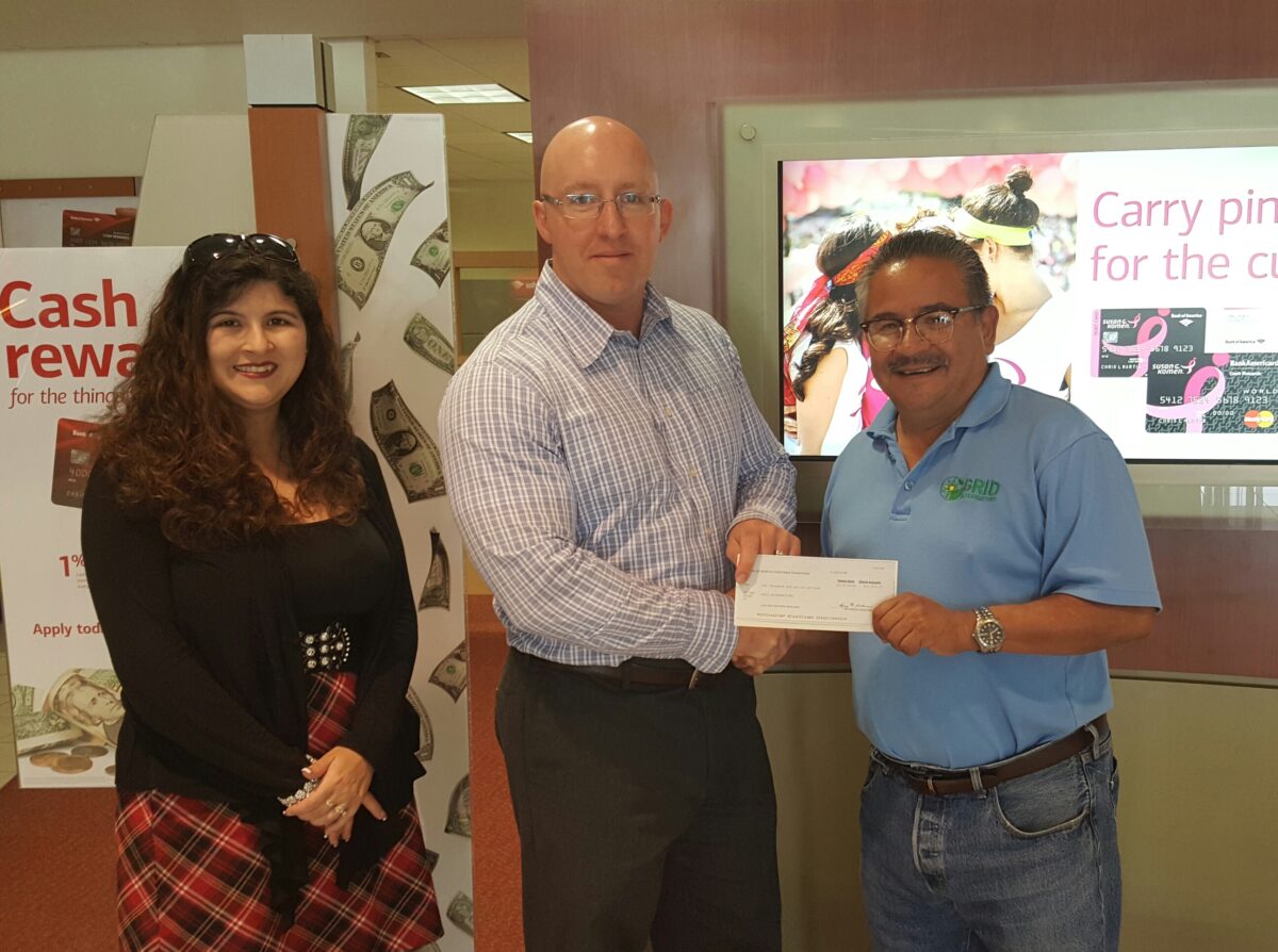 Two bank employees present a check to a man wearing a blue shirt at a community event