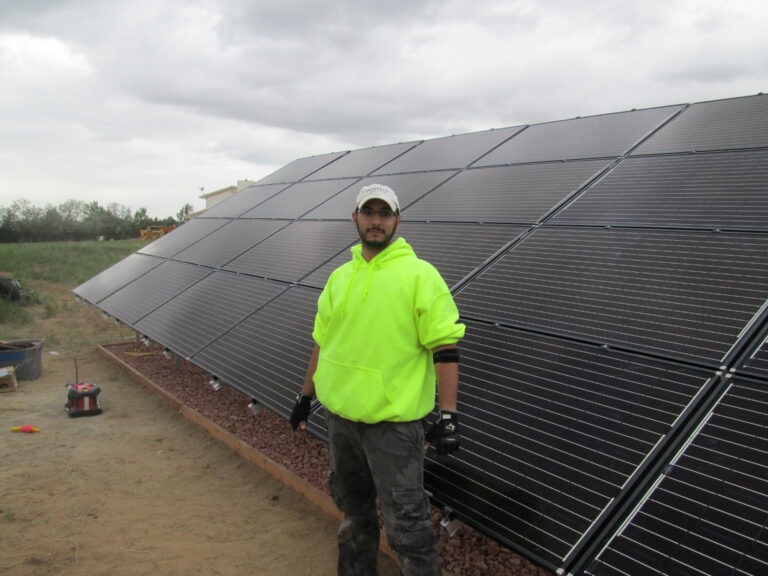 Worker in neon safety vest standing before large solar panel array installation
