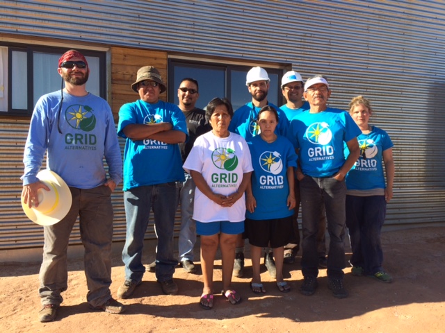 Group of volunteers wearing GRID shirts and hats standing together at a solar installation site